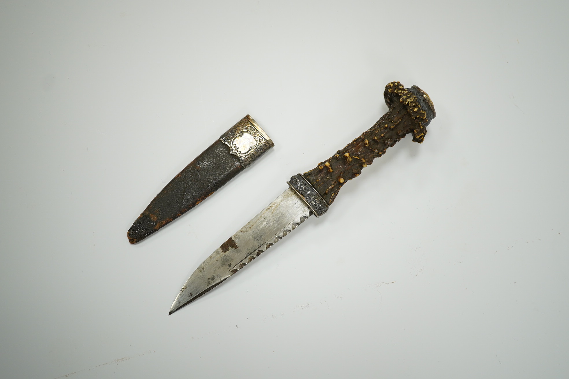 A late 19th century Scottish traditional sgian dubh with foiled glass mounted deer antler handle, and silver coloured metal mounts with thistles in relief, blade 10cm. Condition - fair, missing chape.